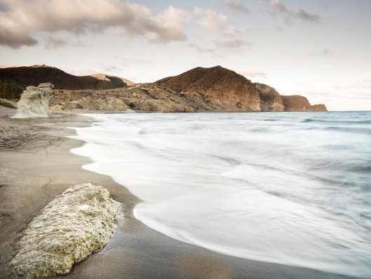Beach with dark sand and cliffs in the background in evening mood    	